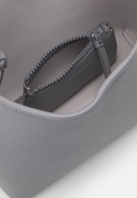 Harmaa nahkalaukku, jossa on vetoketjullinen tasku helmellä varustetulla vetoketjulla. Sileä pinta, pyöristetyt reunat, minimaalinen näkyvä metalliosuus.
