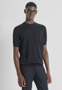 Maglione nero a maniche corte, design a girocollo, texture liscia, con polsi e orlo ribattuti. Indossato con pantaloni neri.