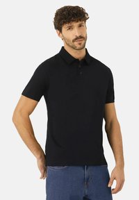 Musta lyhythihainen polo-paita, joka on valmistettu puuvillasta. Tässä paidassa on kaulus, kolme nappia ja kapea muotoilu. Paita on yhdistetty sinisiin farkkuluihin.