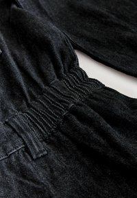 Black denim fabric with a soft texture and slight stretch. Features gathered waistband, accentuated seams, and a casual design.