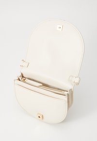 Piccola borsa a tracolla in pelle crema con chiusura in oro, pattina aperta che mostra una tasca interna con zip e bordi cuciti.
