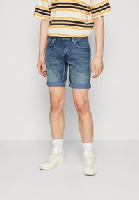 Shorts de mezclilla en azul claro con corte recto, con puños enrollados. Combinados con una camiseta de rayas de manga corta y zapatillas blancas.