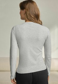 Lys grå langærmet top med ribbet struktur og rund halsudskæring, der har et tætsiddende design, der snævrer ind ved taljen.