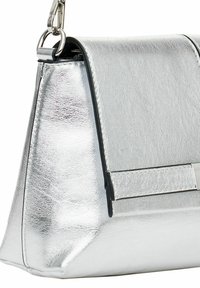Sac à main en métal argenté avec une forme structurée, surface texturée, accents noirs et une bandoulière amovible. Présente des détails en matériel minimalistes.