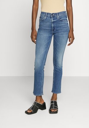 Vaqueros de un azul claro con un diseño de pierna recta, hechos de tela de mezclilla. Presentan un ligero desgastado y un dobladillo sin rematar. Combinados con sandalias negras gruesas.