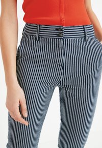 Pantaloni a righe blu navy e bianchi con una vita alta, dotati di due bottoni e tasche laterali. Il tessuto ha una consistenza liscia.