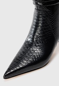 Stivaletto alla caviglia in finta pelle nera con punta affusolata e motivo testurizzato a rettile. Presenta una finitura lucida e una silhouette elegante.