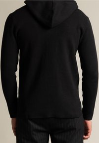 Sudadera negra de punto con una textura suave, capucha en la parte trasera y mangas largas ajustadas. Combinada con pantalones a rayas.