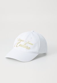 White baseball cap made of cotton with a curved brim. Features gold embroidered text "Versace Jeans Couture" on the front.