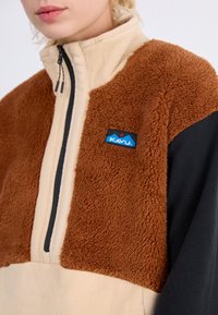 Pólder KAVU de forro polar con media cremallera, que presenta paneles en tonos marrón, negro y beige, tela texturizada y un parche con el logo en el pecho.
