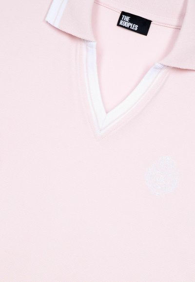 Lichtroze polo shirt met een V-hals, witte kraagaccenten en een geborduurd logo aan de linkerkant. Gemaakt van een gestructureerde stof.