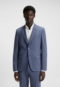 Giacca da abito azzurro chiaro con rever a soffietto, due tasche frontali e chiusura con un solo bottone, abbinata a una camicia bianca. Tessuto strutturato.