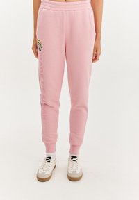 Svetloružové tepláky s elastickým pásom a manžetami na členkoch, s obrázkom kresleného charakteru a textom "VYROBENÉ Z CUKRU" v tučnom písme.