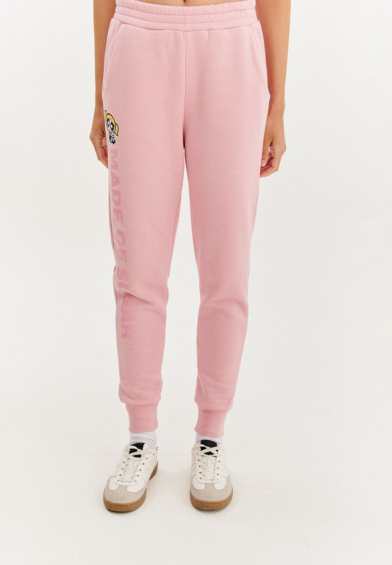 Svetloružové tepláky s elastickým pásom a manžetami na členkoch, s obrázkom kresleného charakteru a textom "VYROBENÉ Z CUKRU" v tučnom písme.