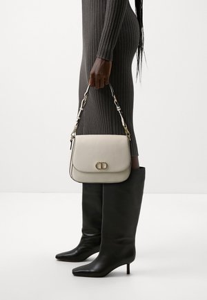 Béžová kožená kabelka s klopou, zdobená zlatým logem a popruhem s řetízkovým akcentem. Černé kozačky ke kolenům s špičatou špičkou.