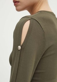 Top lavorato a maglia verde oliva con spalle scoperte e dettaglio di bottone argentato sulla manica. Il tessuto ha una texture liscia.