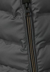 Schwarze Steppweste mit einem zentralen Reißverschluss in Goldfarbe und strukturiertem Stoff, der ein gestepptes Design zeigt.