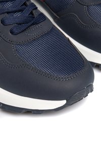 Mereviste sinised sportjalatsid tekstuuriga võrkkangast pealispinnaga, siledate sünteetiliste ülemistega, valge vaheosa ja musta kummist välispinnaga, millel on haardemuster.