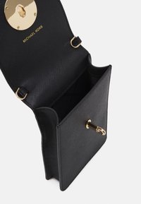 Černá kožená kabelka s texturovaným povrchem, zlatým kováním a kulatým zámkem na uzavření. Interiér není podšitý a má jedinou přihrádku.
