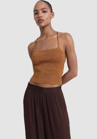 Smeđi pleteni crop top s tankim trakama, koji ima teksturirani uzorak. Uparen s labavim, tamnosmešim hlačama visokog struka. Jednostavan dizajn.