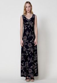 Robe maxi en tissu élastique, présente un fond marine avec des motifs floraux en argent et rouge. Décolleté en V et design sans manches.