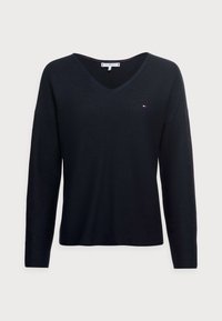 Pull-over en V à manches longues bleu marine, avec une texture côtelée, arborant un petit logo sur la poitrine. Tissu doux, coupe décontractée et manches larges.