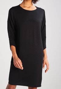 Robe noire en tissu doux, avec un col rond, des manches trois-quarts et une coupe décontractée qui arrive au-dessus des genoux.