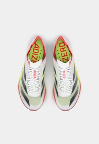Baskets de sport blanches et grises avec des rayures noires, accents rouges vif et semelles jaunes. Présente un dessus en mesh et un logo "ADIZERO" audacieux.