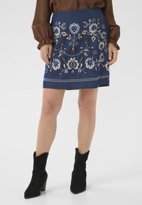 Jupe en jean noir ornée d'une broderie florale colorée en bleu, blanc et marron. Accentuée par une bande cousue à l'ourlet.