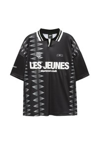 Polo noir à manches courtes avec motif géométrique triangulaire blanc, texte "LES JEUNES département créatif" en blanc gras, et col rayé.
