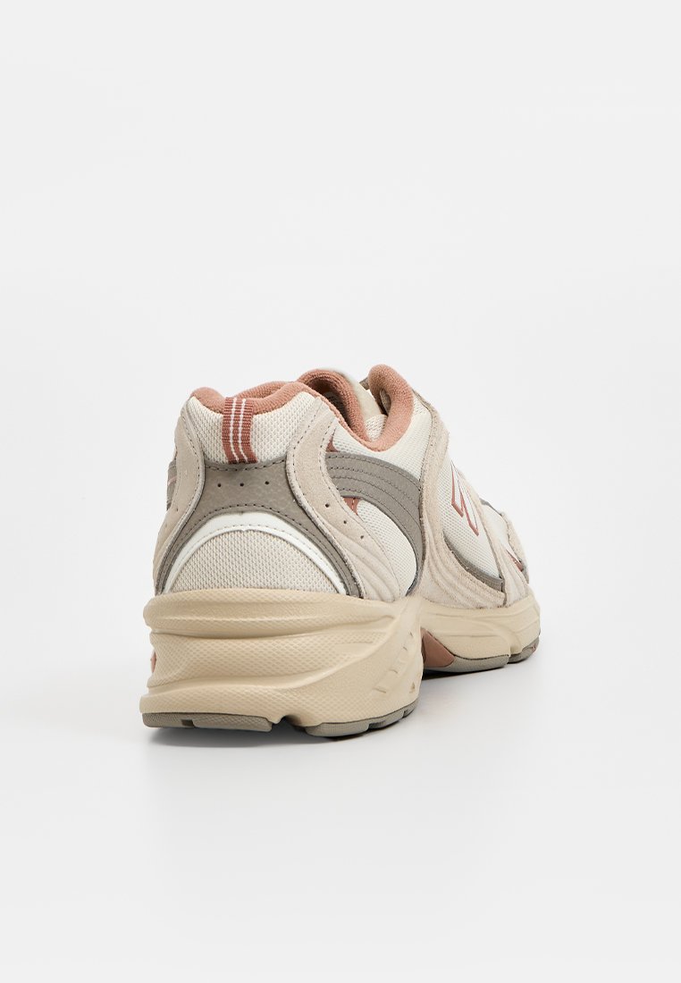 Baskets de sport beige et gris clair avec une tige en maille texturée, un col rembourré et une semelle en caoutchouc. Inclut des accents orange contrastants.