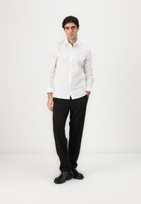 Weißes langärmliges Hemd mit Knopfleiste und taillierter Passform, kombiniert mit schwarzen Hosen und eleganten schwarzen Schuhen. Glatter Stoff mit klassischem Kragen.