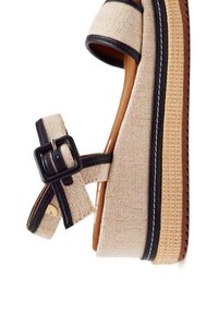 Sandalo in tessuto beige con bordi neri, suola spessa e piattaforma, e cinturino alla caviglia regolabile con fibbia quadrata. Dettagli di superficie testurizzata.