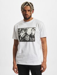 Fehér pamut póló, melyen fekete-fehér grafikai nyomat látható két személlyel, alatta "BEASTIE BOYS" felirattal. Kerek nyak, rövid ujjak.