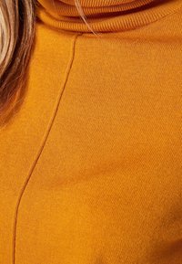 Mustard yellow turtleneck sweater made from ribbed knit fabric, featuring a high collar and a seamless design with vertical stitching.
