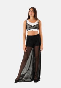 Pantaloni ampi a strati neri e trasparenti con una finitura testurizzata, abbinati a un crop top bianco aderente e a una sovrapposizione in rete nera, dotati di un design con schiena a X.