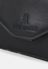 Clutch in ecopelle nera con logo "STEVE MADDEN" in rilievo, design con patta angolare e dettagli di cucitura a contrasto. Texture liscia.