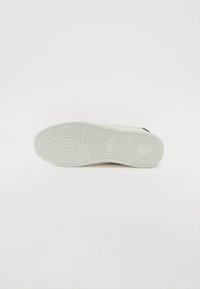 Hvit sneaker med en teksturert gummisåle som har spor og sirkulære mønstre, designet for godt grep og holdbarhet.
