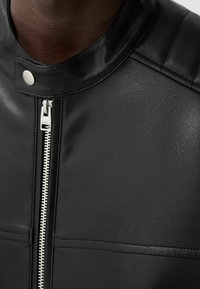 Giubbotto in pelle nera con colletto rialzato, zipper argentato e dettagli trapuntati sulle spalle, che mette in mostra una finitura strutturata e un design elegante.