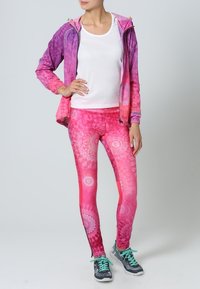 Completo da attrezzatura attiva che presenta una giacca leggera con zip dai colori degradé viola a rosa; leggings aderenti con un motivo mandala in tonalità di rosa.