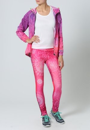 Ensemble de vêtements de sport comprenant une veste légère à fermeture éclair dégradée allant du violet au rose ; leggings ajustés avec un motif mandala dans des tons de rose.
