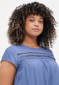 Blue blouse featuring short sleeves, lace detailing across the chest, and a round neck with a scalloped trim. Soft, flowing fabric.
