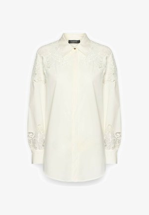 Crèmewitte blouse met lange mouwen, kantdetails op de schouders en manchetten, puntige kraag en verborgen knopen aan de voorkant.