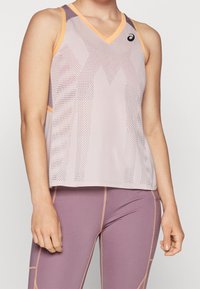 Canottiera sportiva a V in lilla chiaro con dettagli arancioni e motivo in rete, abbinata a leggings viola coordinati.