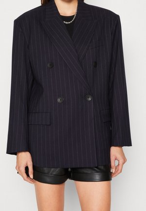 Double-breasted navy pinstripe blazer with black buttons, notched lapels, and side pockets. Textured fabric, slightly oversized fit.