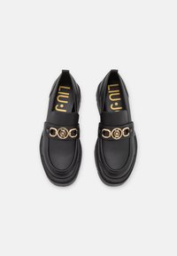 Černé kožené loafers s masivní podrážkou, zlatým řetízkovým kováním vepředu a strukturovaným svrškem. Logo ve zlaté barvě na vnitřní straně.