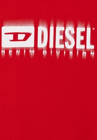 T-shirt in cotone rosso con un audace logo "DIESEL" stampato in bianco e il testo "DENIM DIVISION", che si fonde perfettamente con il tessuto.