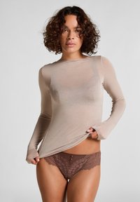 Nude lange mouwen top in doorschijnende stof, gecombineerd met bruin kanten slipje met twee kleine knopen aan de voorkant en geschulpte randen.