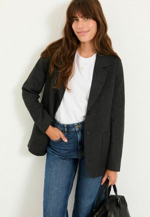 Dunkelgrauer Wollblazer mit Revers, Ein-Knopf-Verschluss und zwei Fronttaschen, kombiniert mit einem weißen T-Shirt und blauen Jeans.