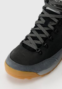 Black and gray hiking shoe with textured suede and synthetic materials, featuring gray laces, metal eyelets, and a gum rubber sole.